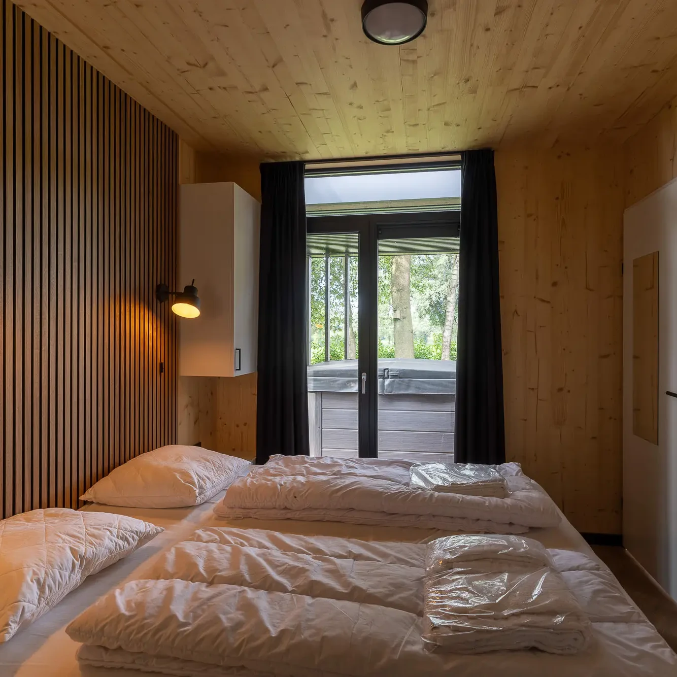 Sfeervolle slaapkamer met houten wanden en plafond in Panorama Lodge Markelo met uitzicht op natuur