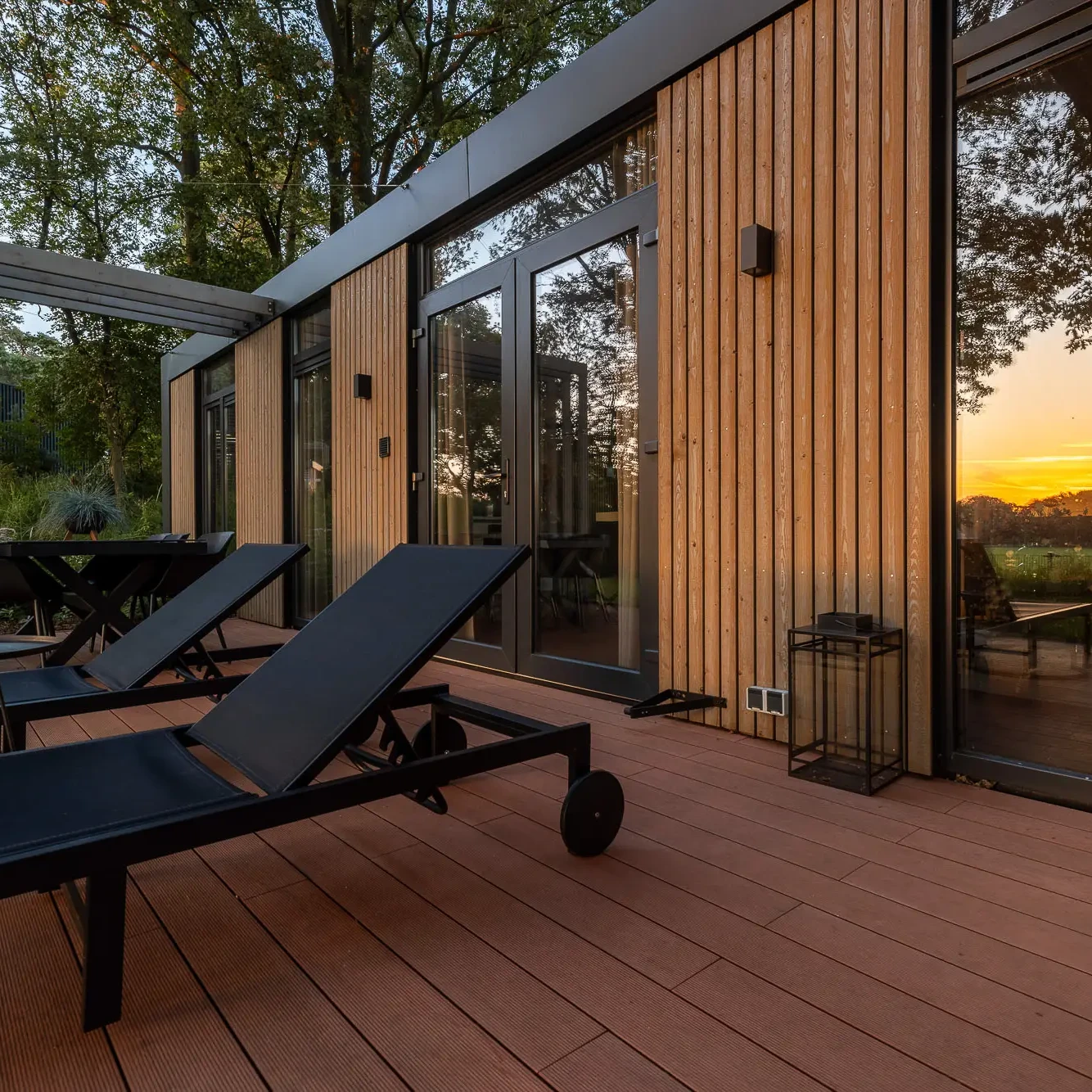 Luxe houten terras met ligbedden bij Panorama lodge Markelo tijdens zonsondergang