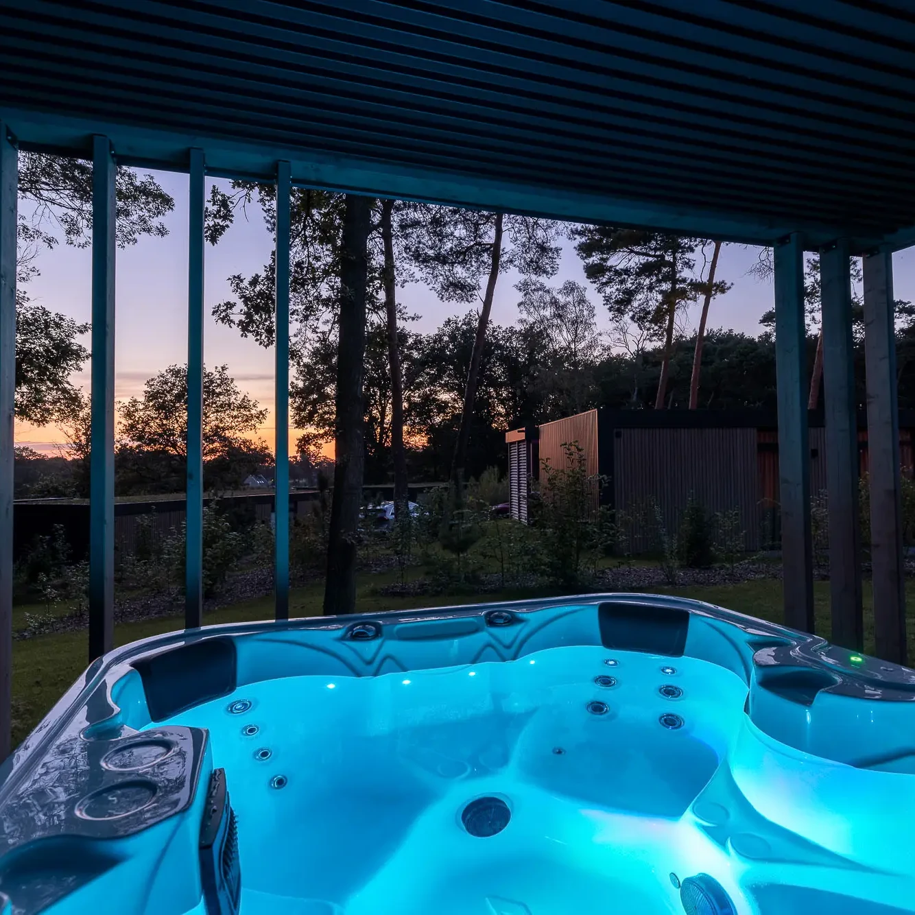 Verlichte jacuzzi met turquoise water bij schemering op Zicht op Twente Lodges in Markelo