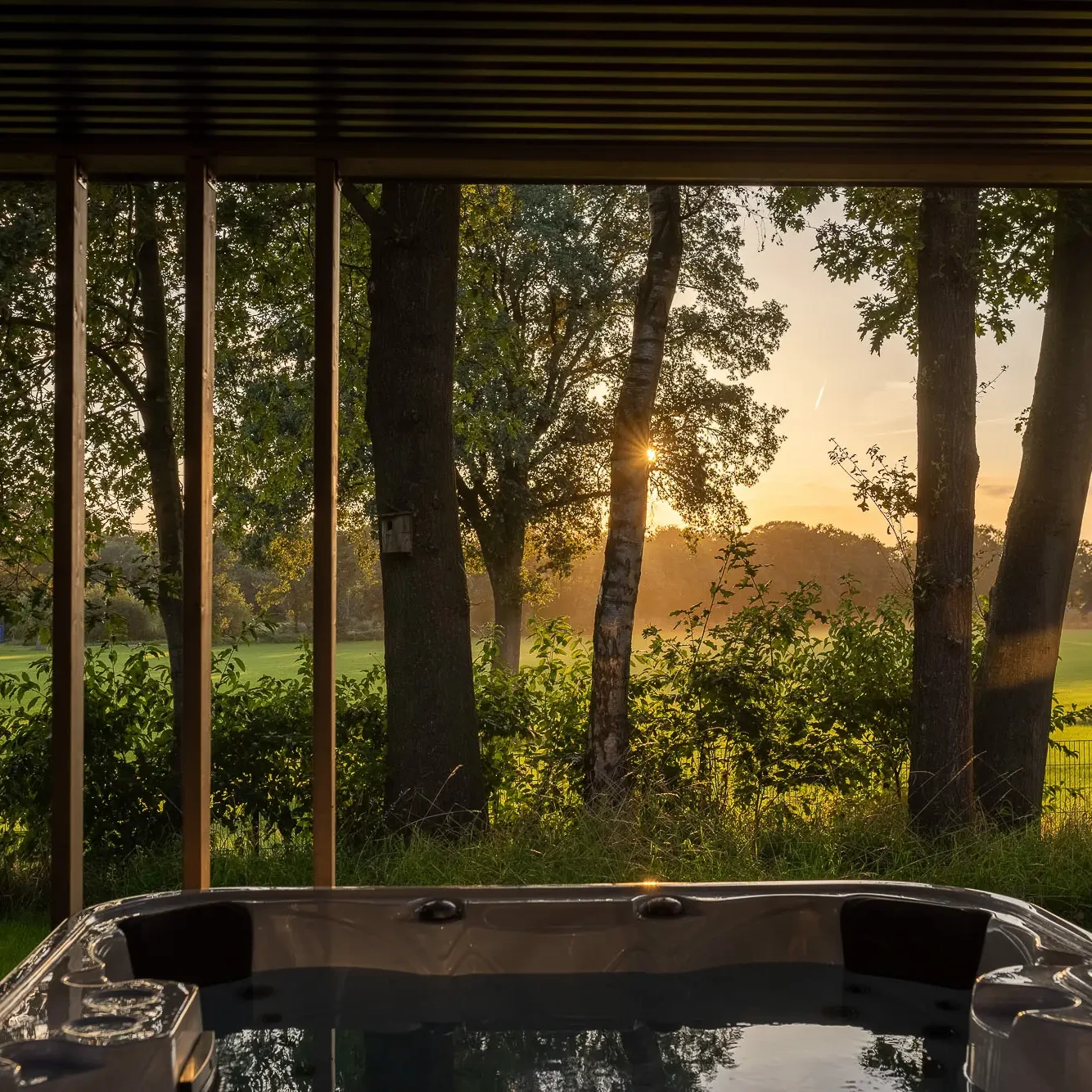 Bubbelbad met uitzicht op groene weilanden en bomen bij zonsondergang in Markelo