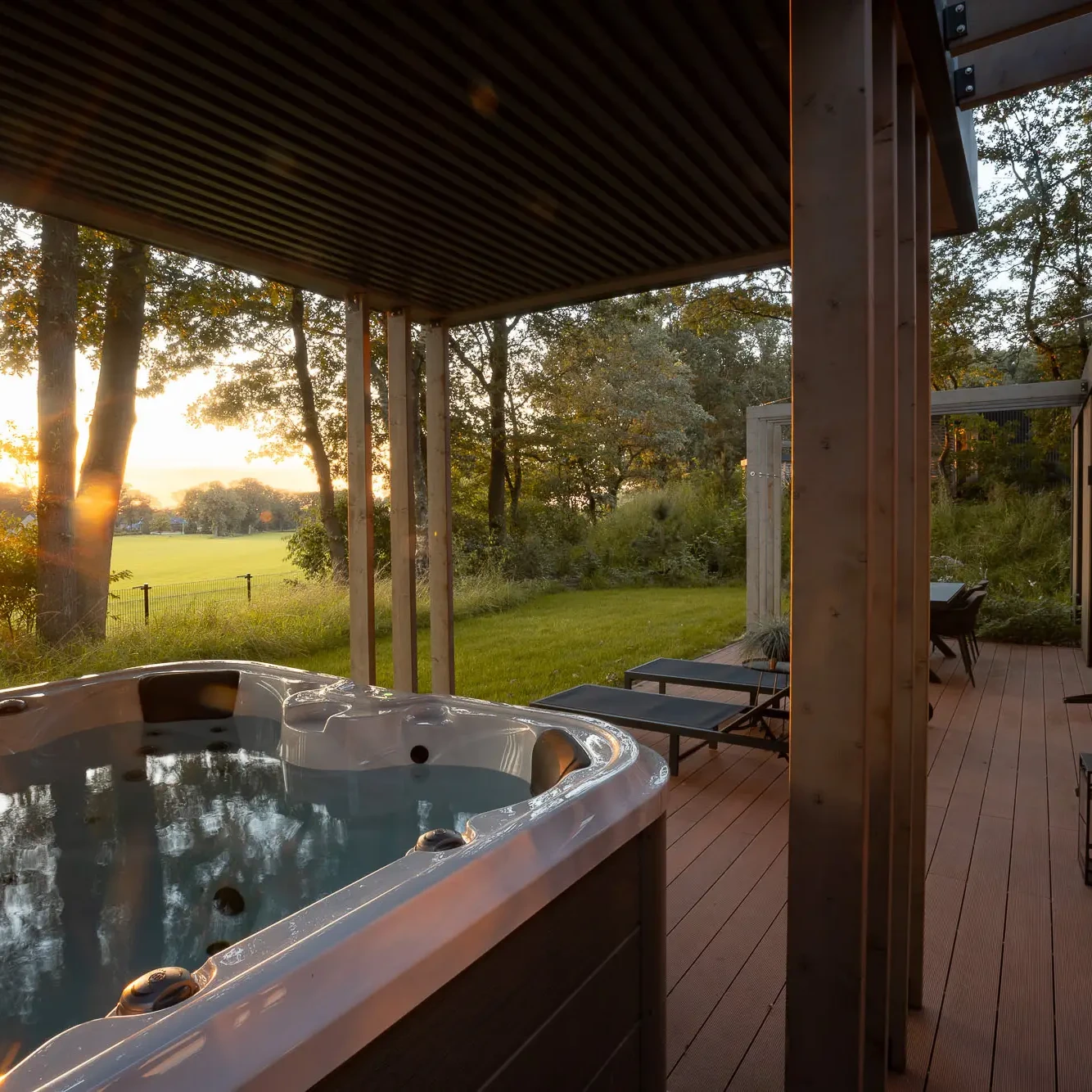 Luxe jacuzzi op houten terras met uitzicht op Twentse natuur bij zonsondergang