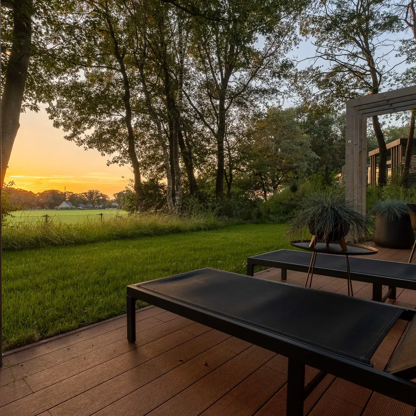 Luxe ligbedden op houten terras van Panorama Lodge met uitzicht op Twentse natuur bij zonsondergang
