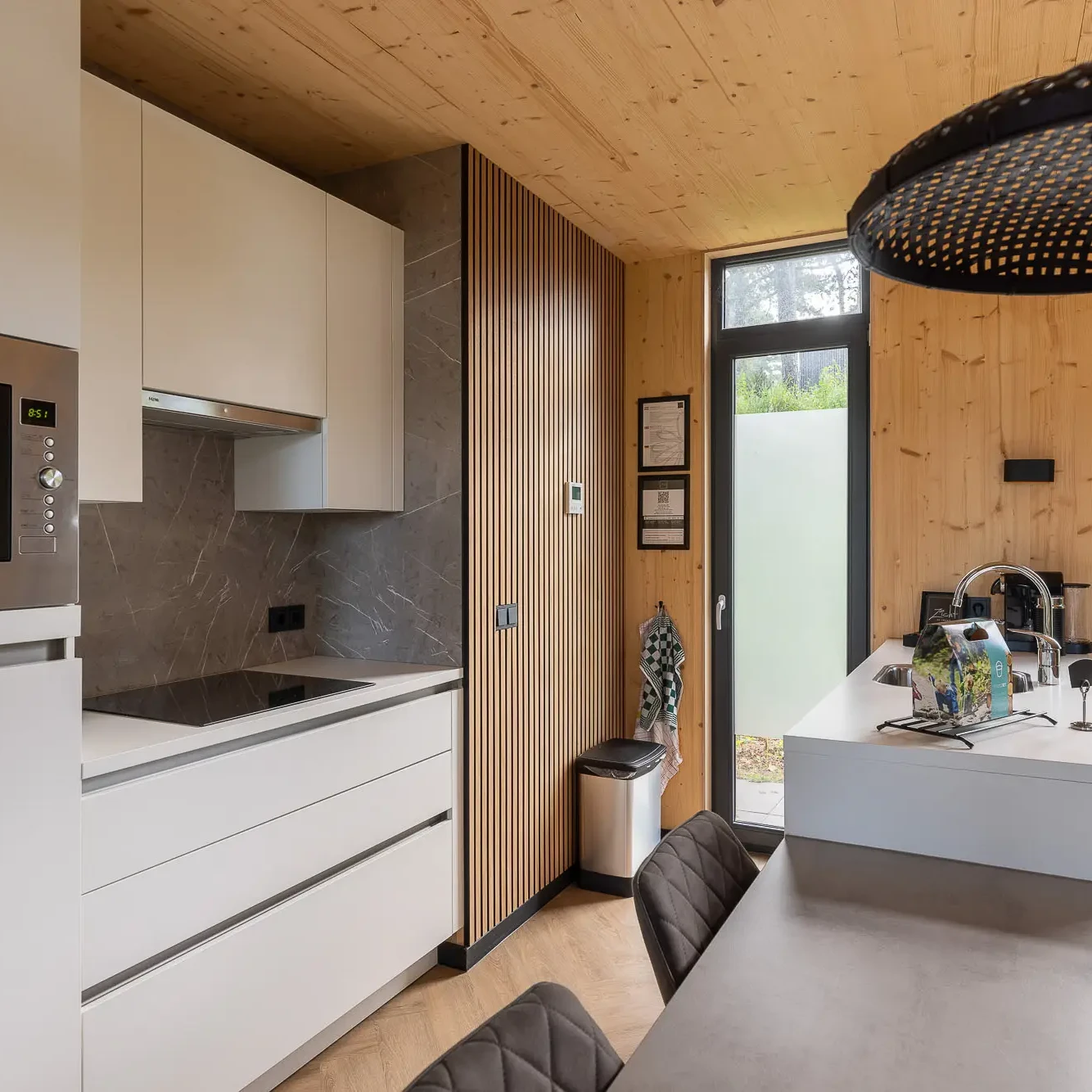 Moderne keuken met witte kasten, houten plafond en grijze marmeren spatwand in Panorama lodge Markelo