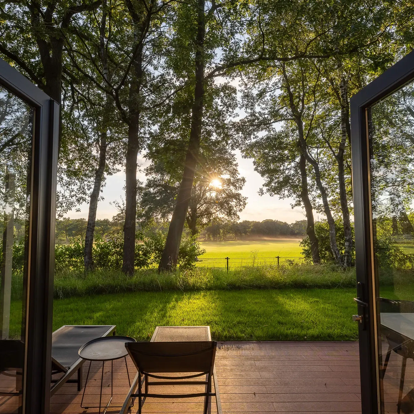 Uitzicht vanaf terras Panorama Lodge op groene weilanden en bomen bij zonsondergang in Markelo