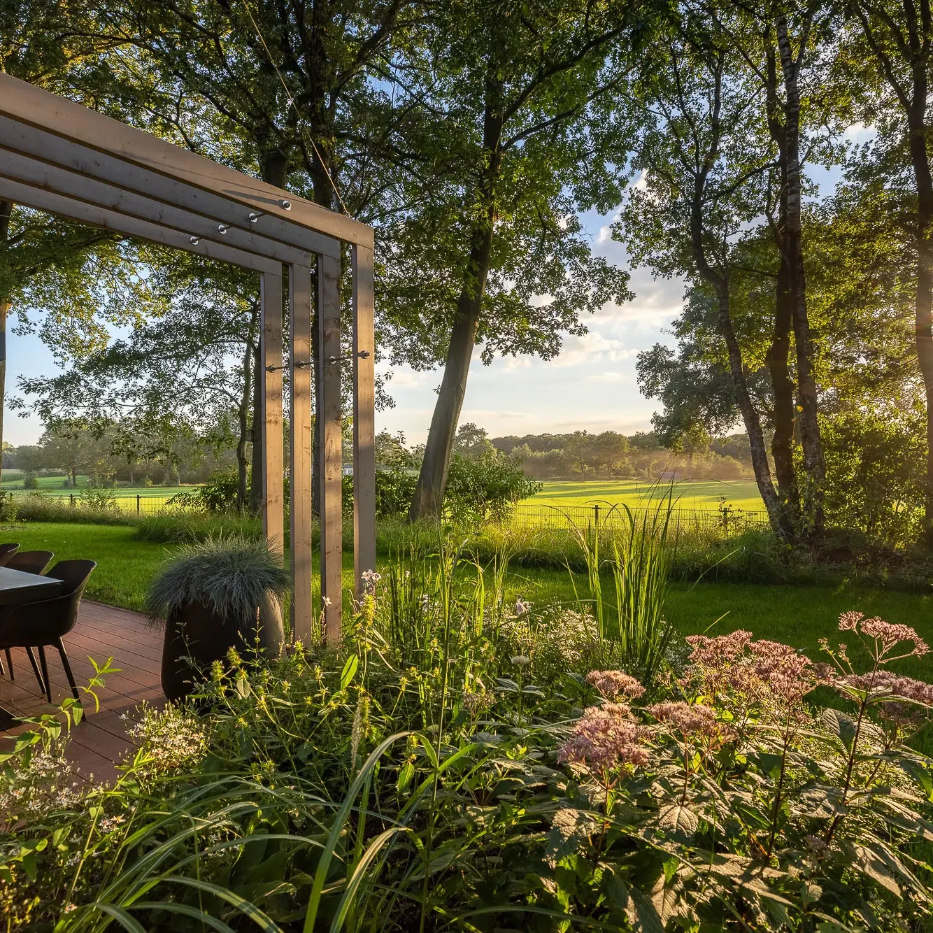 Overdekt terras met eethoek en uitzicht op groene weilanden in Twente bij zonsondergang